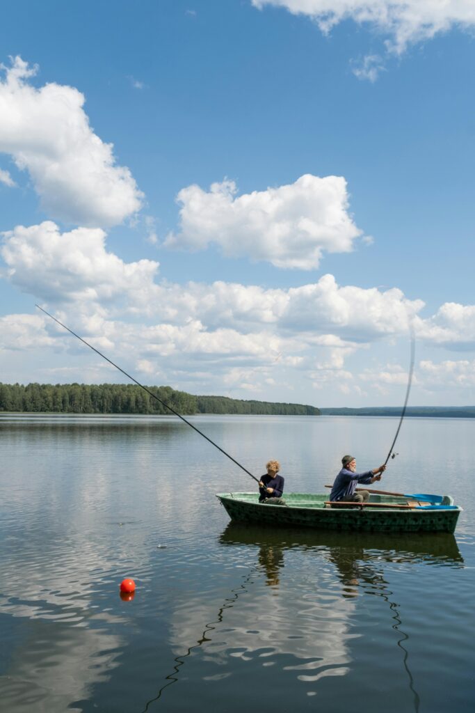 A peaceful scene of a father and son fishing in a small boat on a calm lake under a blue sky.